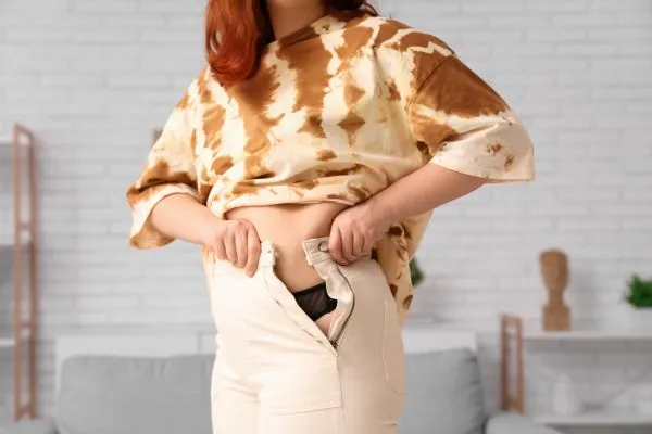 Image of woman trying to do her trousers up after pregnancy weight gain Liverpool