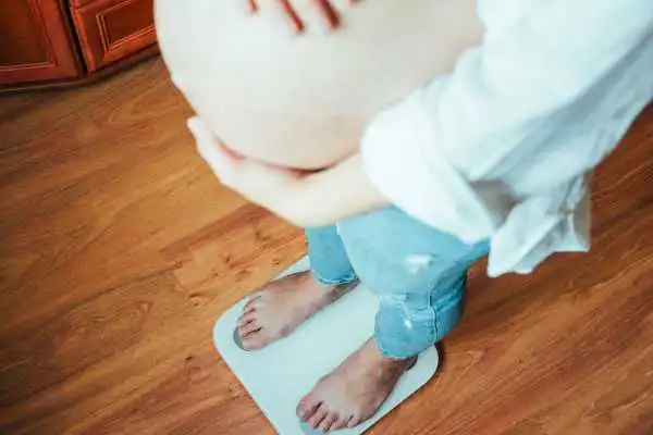 Image of woman weighing herself and experiencing weight gain through pregnancy Liverpool